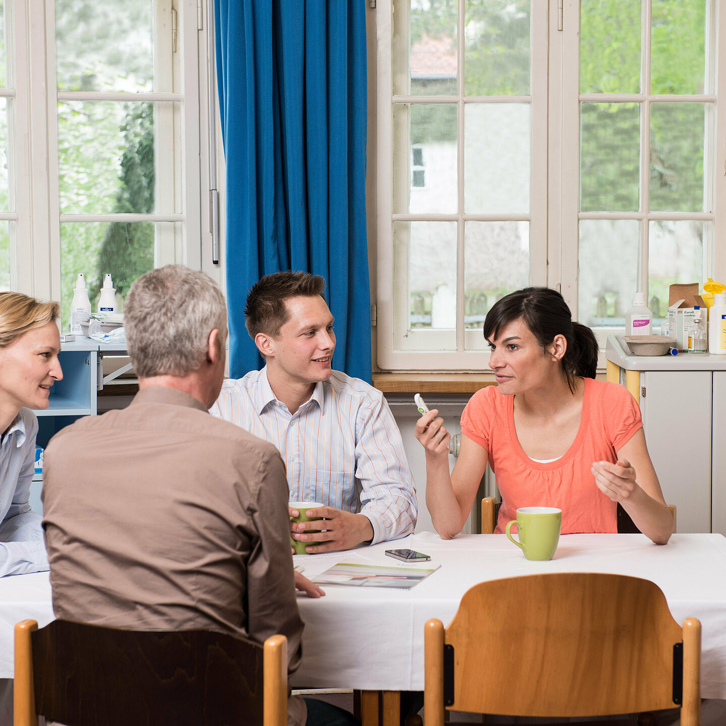Vier Personen sitzen an einem Tisch und besprechen etwas. Im Hintergrund ist medizinisches Material zu sehen.
